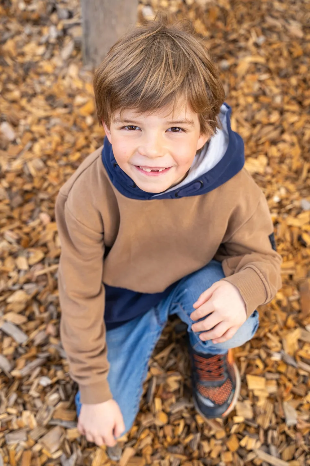 Junge hockt lachend im Herbstlaub