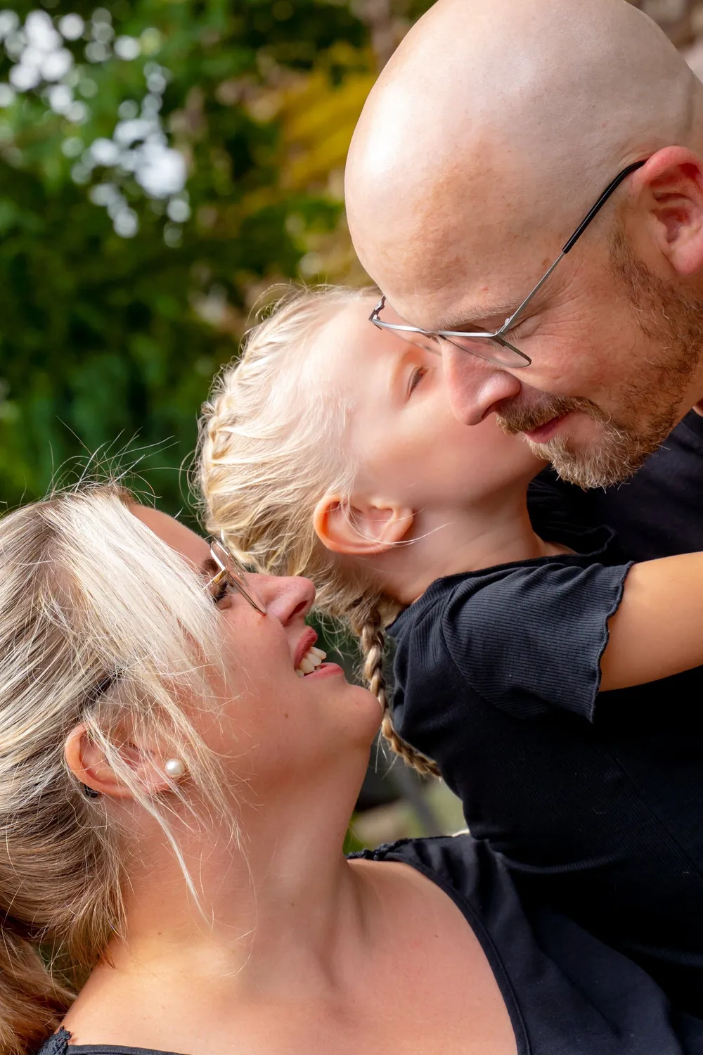 Tochter kuschelt sich lachend an ihre Eltern – Familienshooting im Grünen