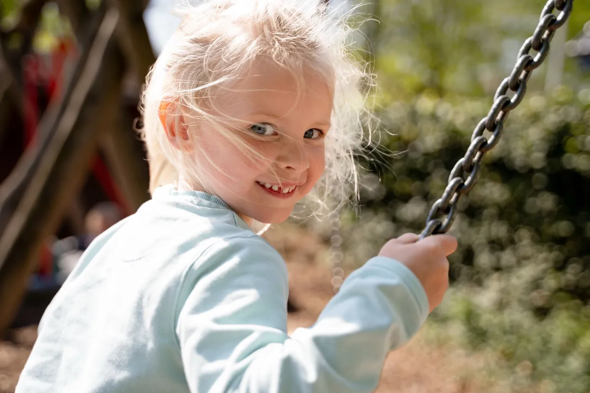 Mädchen lacht beim Schaukeln auf dem Kita-Spielplatz