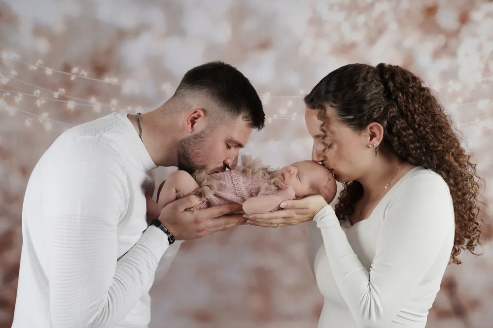 Eltern küssen ihr neugeborenes Baby vor Bokeh-Hintergrund